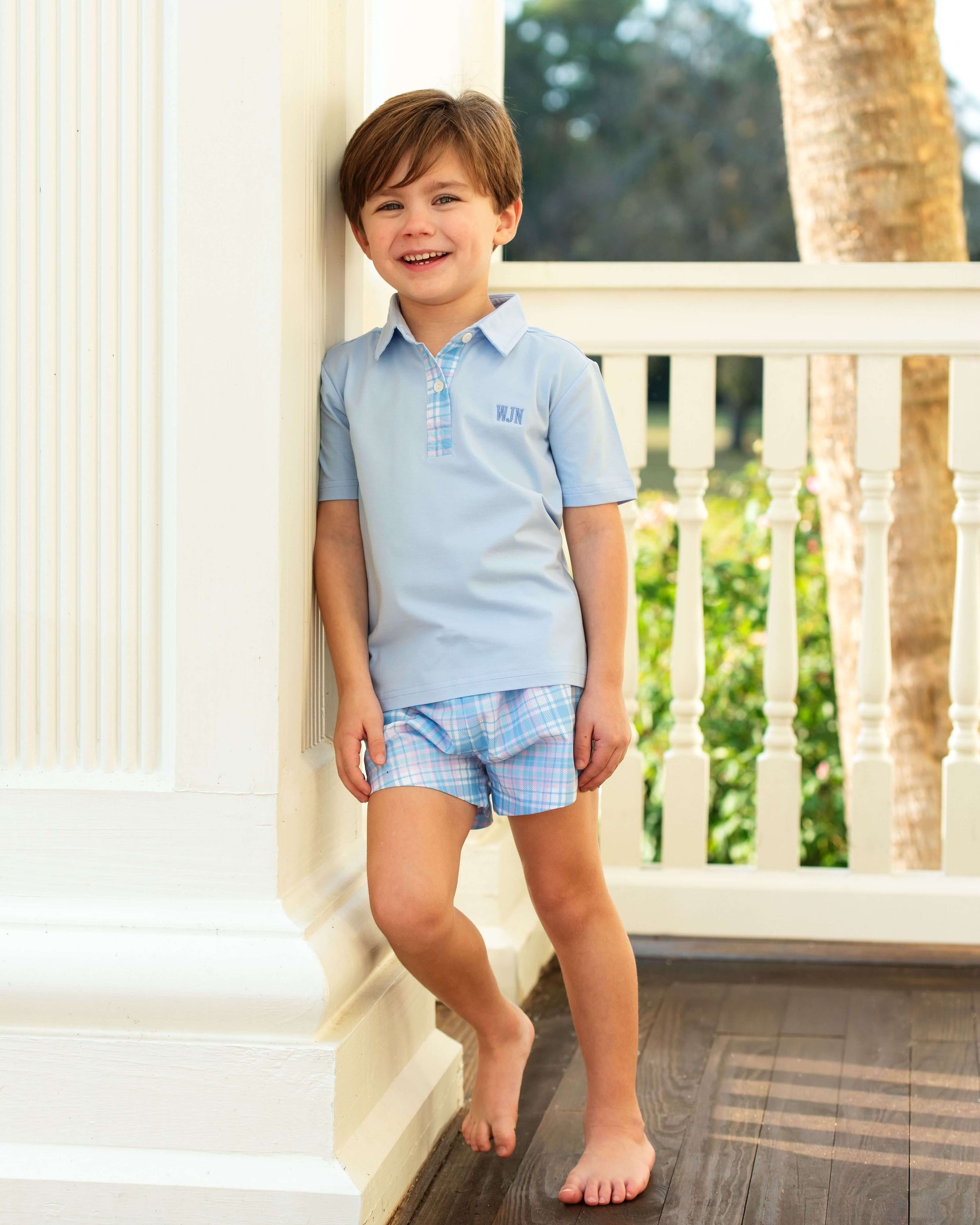 Young boy in a light blue polo shirt and plaid shorts standing on a staircase.