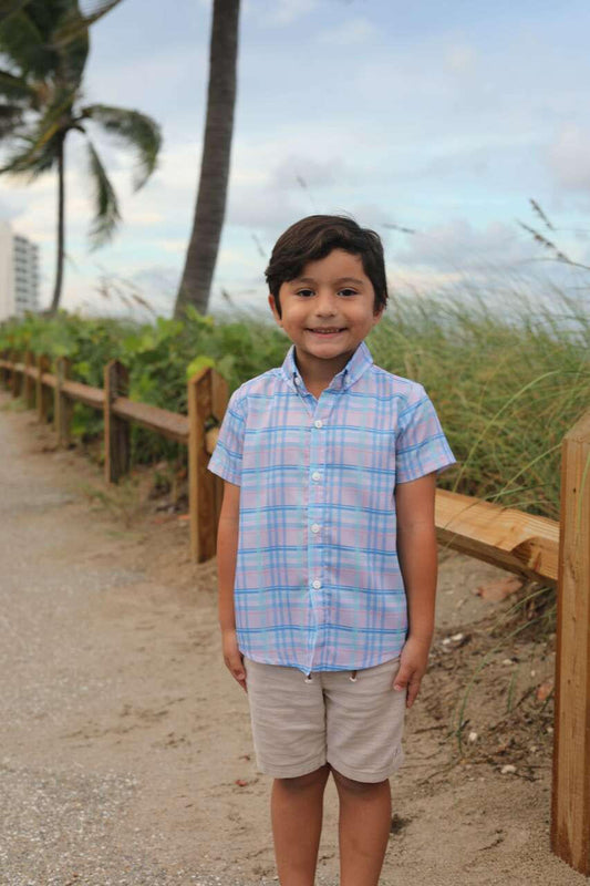 Young boy in a plaid shirt standing on a beach path with palm trees in the background