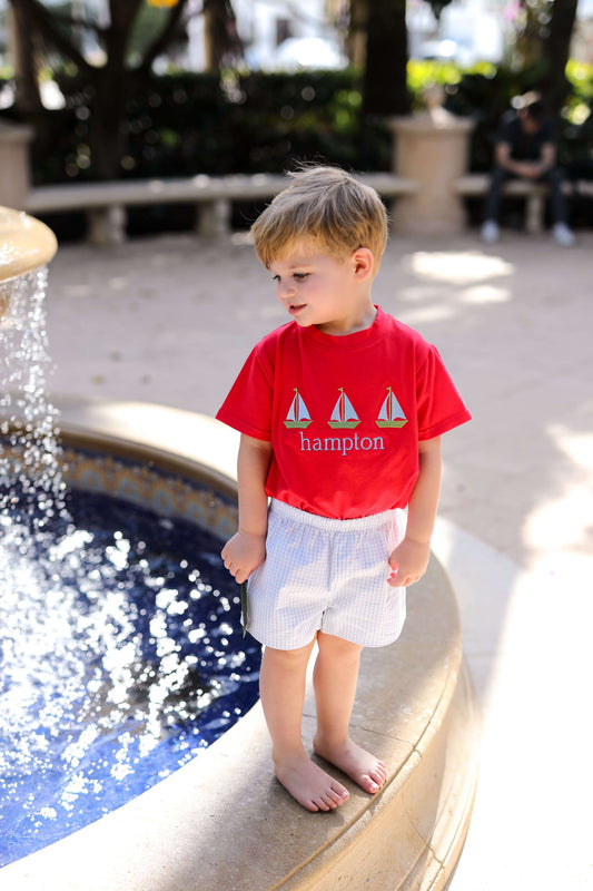 Young boy in a red shirt and white shorts standing by a pool.