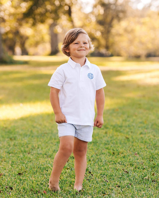 Young boy in a white polo shirt with a monogram standing on grass
