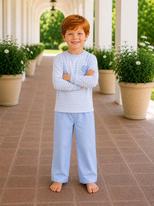 Young boy in light blue pajamas standing on a tiled patio with potted plants in the background