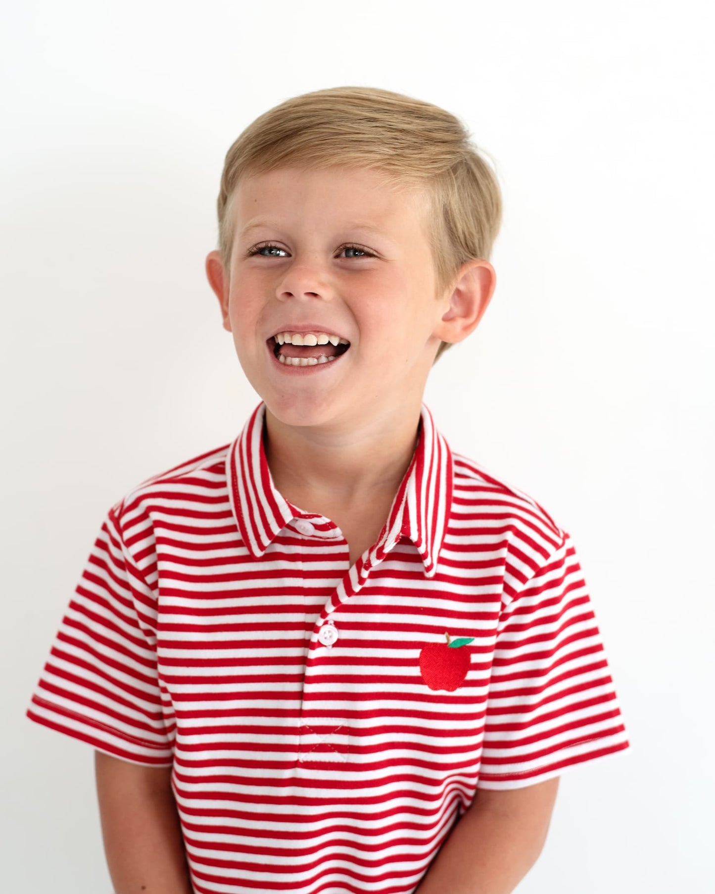 Young boy smiling wearing a red striped shirt with an apple embroidered.