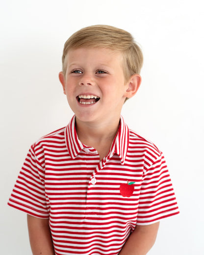 Young boy smiling wearing a red striped shirt with an apple embroidered.