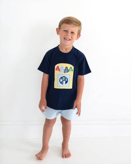 Young boy smiling wearing a school outfit with a crayon box and a monogram. 