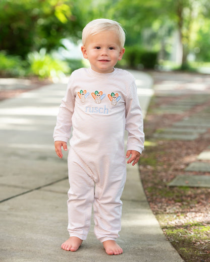 Young boy standing on a sidewalk wearing a khaki outfit with turkeys on it 