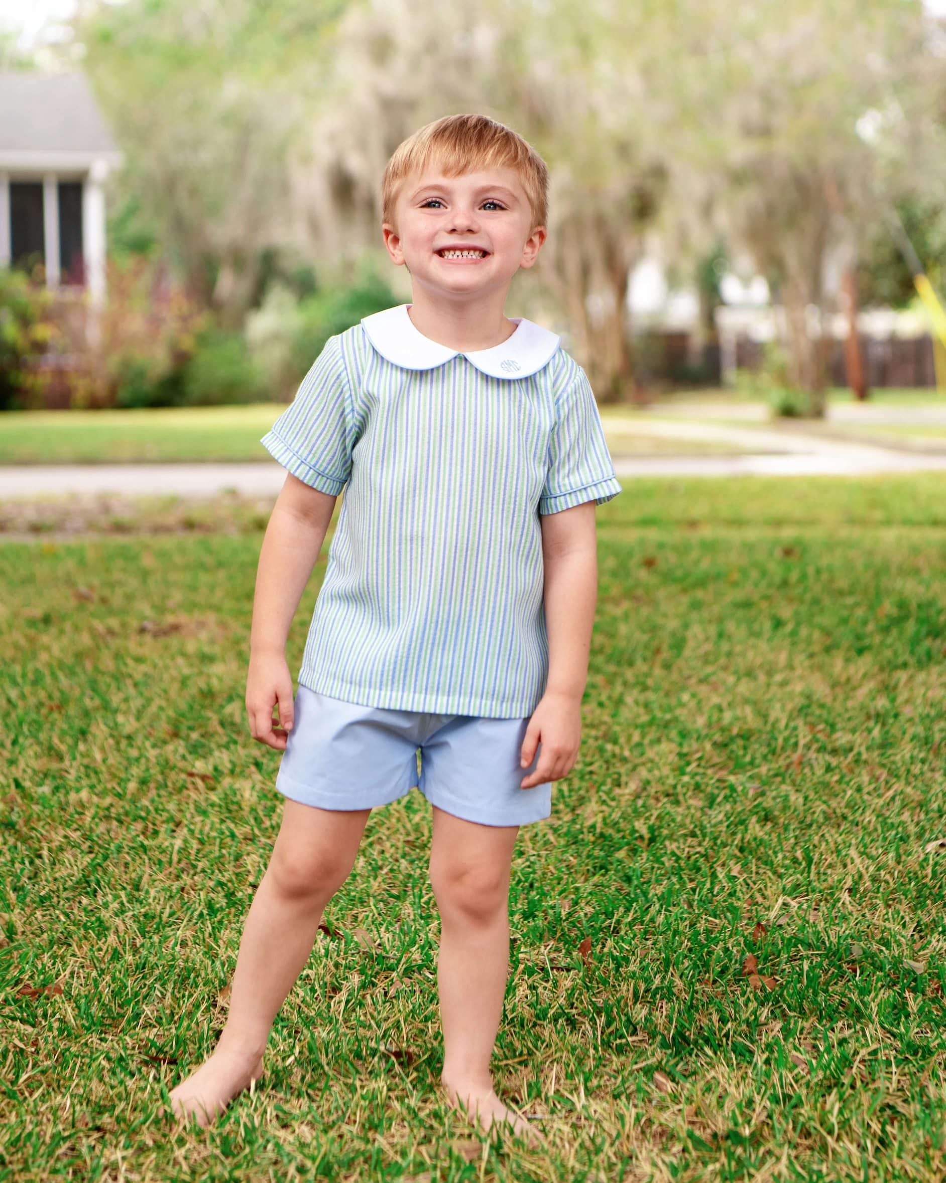 Young boy standing on grass wearing a striped shirt and shorts