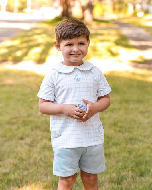 Young boy standing outdoors on grass holding a small toy