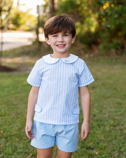 Young boy standing outside wearing a blue striped peterpan short set