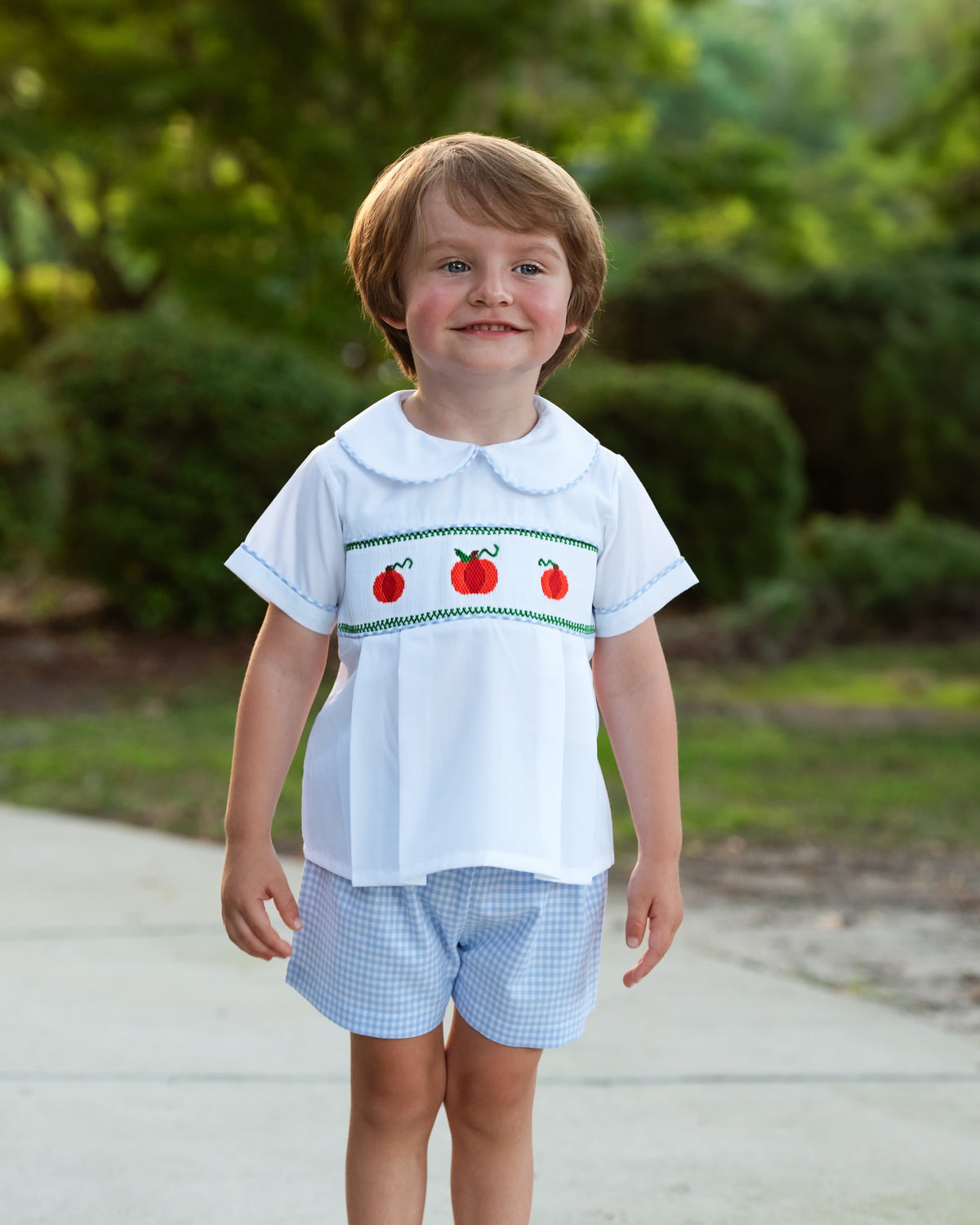 Boy wearing the Blue Gingham Smocked Pumpkin Short Set outdoors
