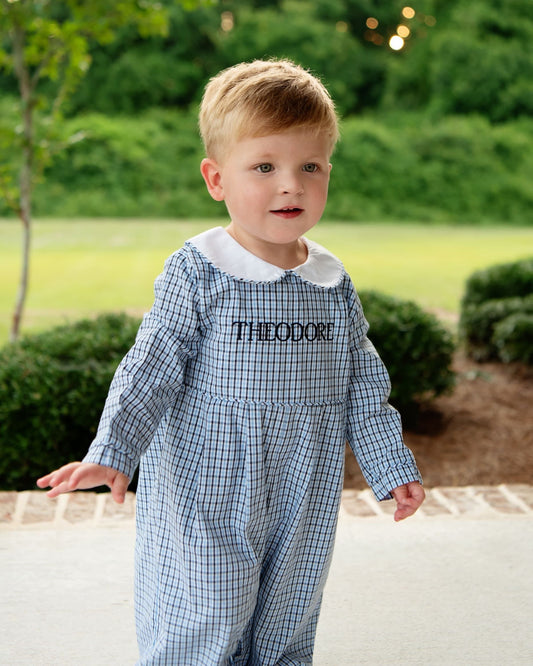 Young boy wearing a blue and navy plaid long romper 