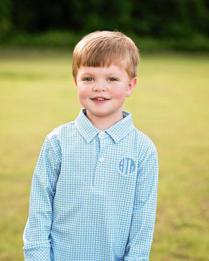 Young boy wearing a blue checkered shirt with monogram in a grassy field