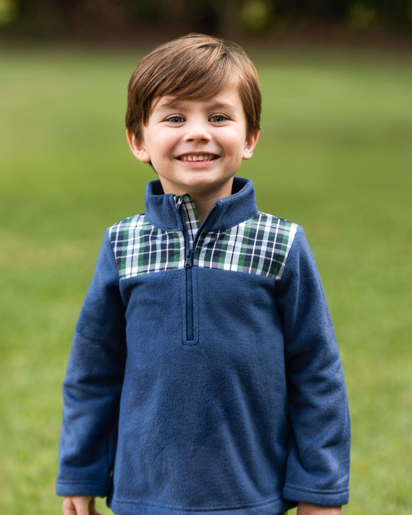 Young boy wearing a blue fleece pullover with plaid accents outdoors.