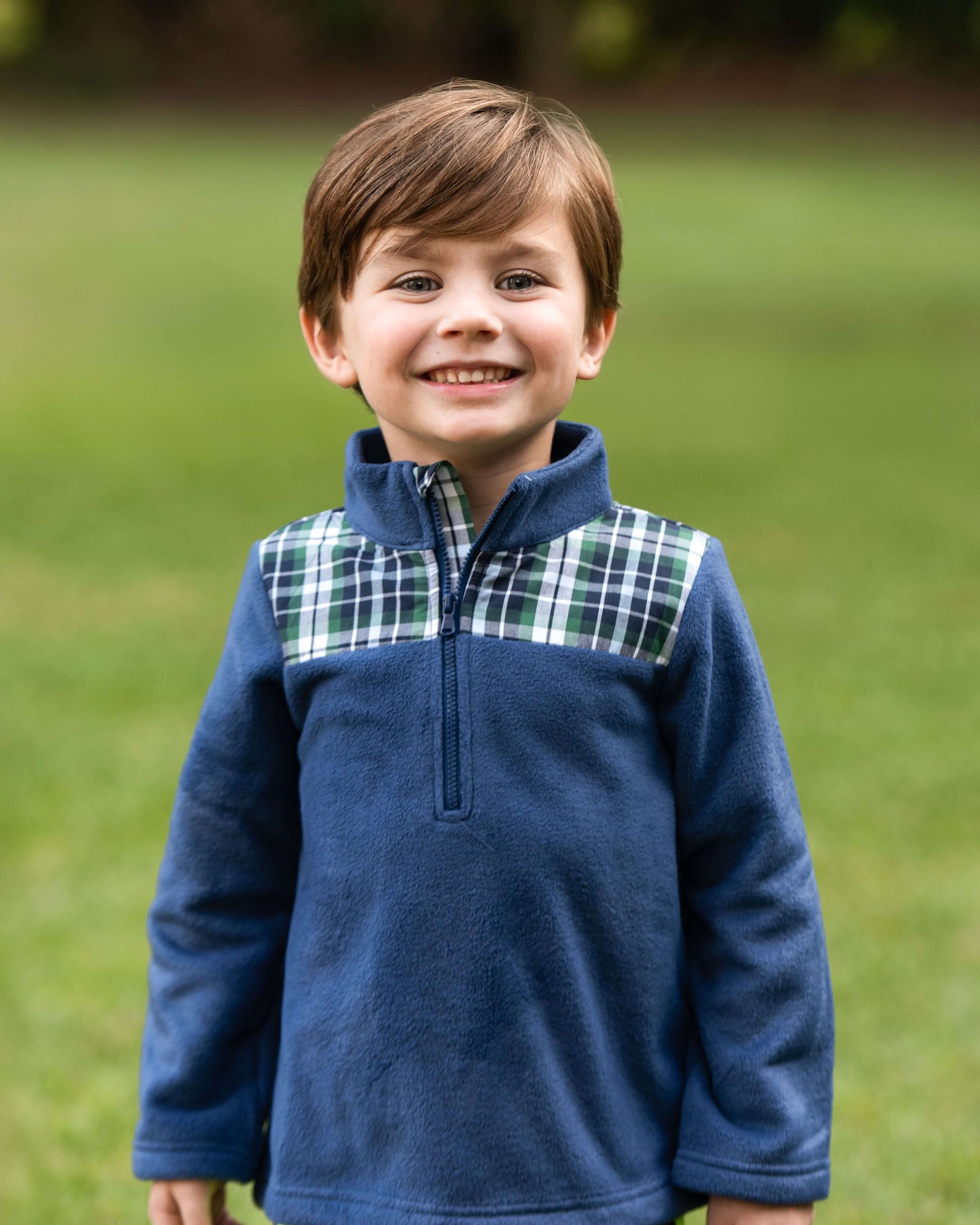 Young boy wearing a blue fleece pullover with plaid accents outdoors.