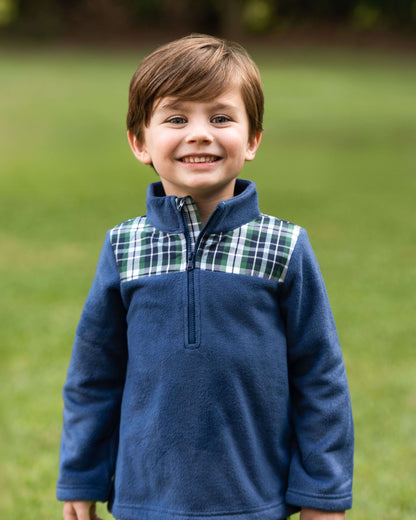 Young boy wearing a blue fleece pullover with plaid accents outdoors.