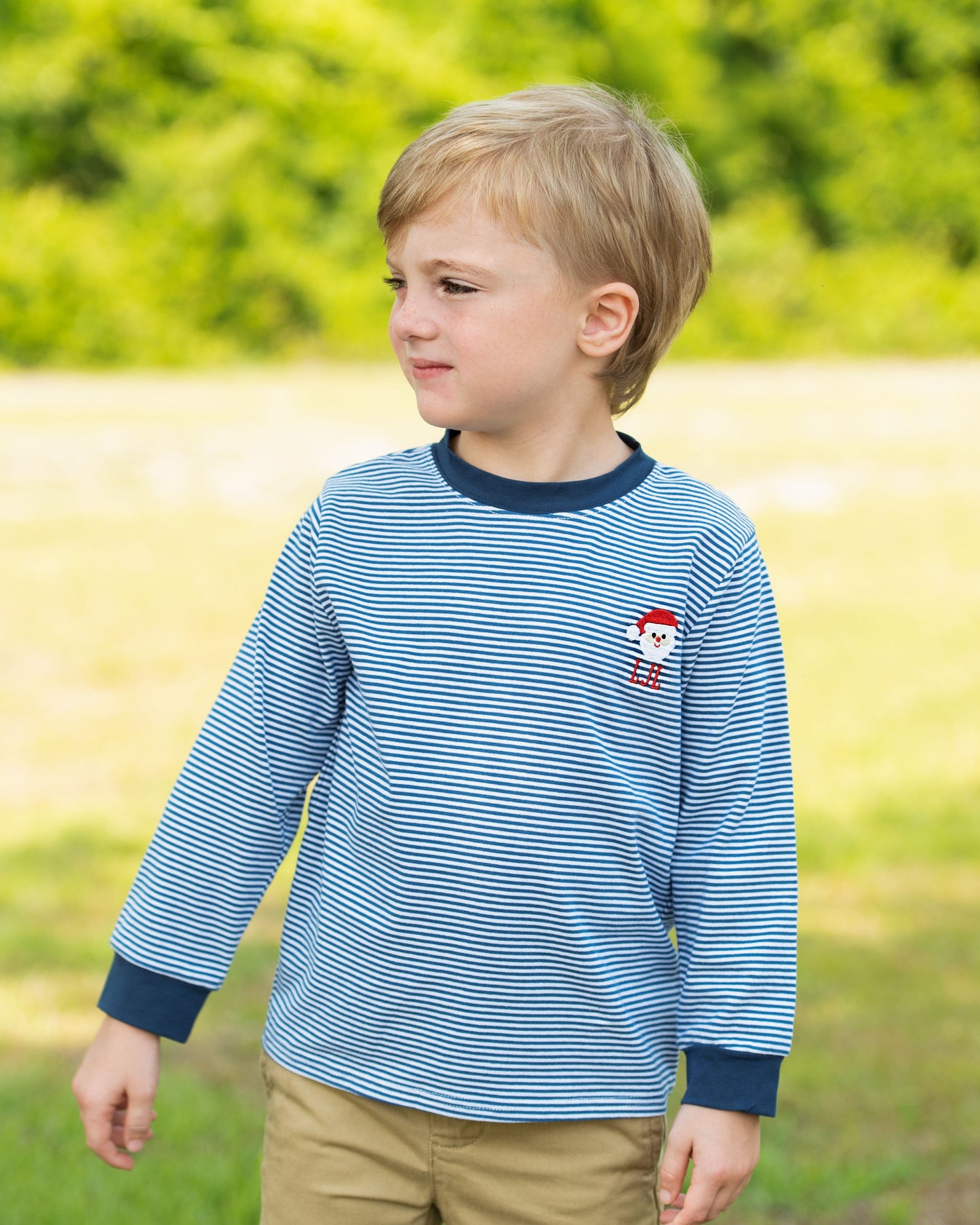 Young boy wearing a blue striped shirt with a red character on it, standing in a grassy field.