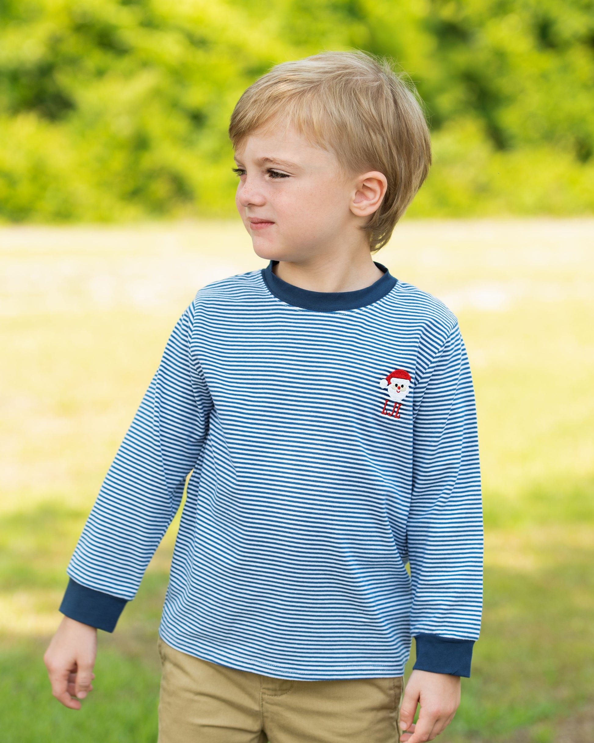 Young boy wearing a blue striped shirt with a red character on it, standing in a grassy field.