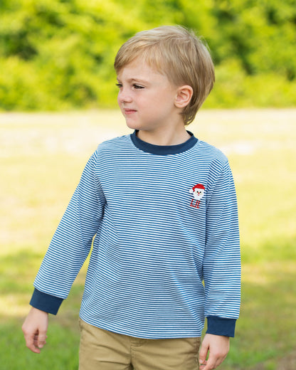 Young boy wearing a blue striped shirt with a red character on it, standing in a grassy field.