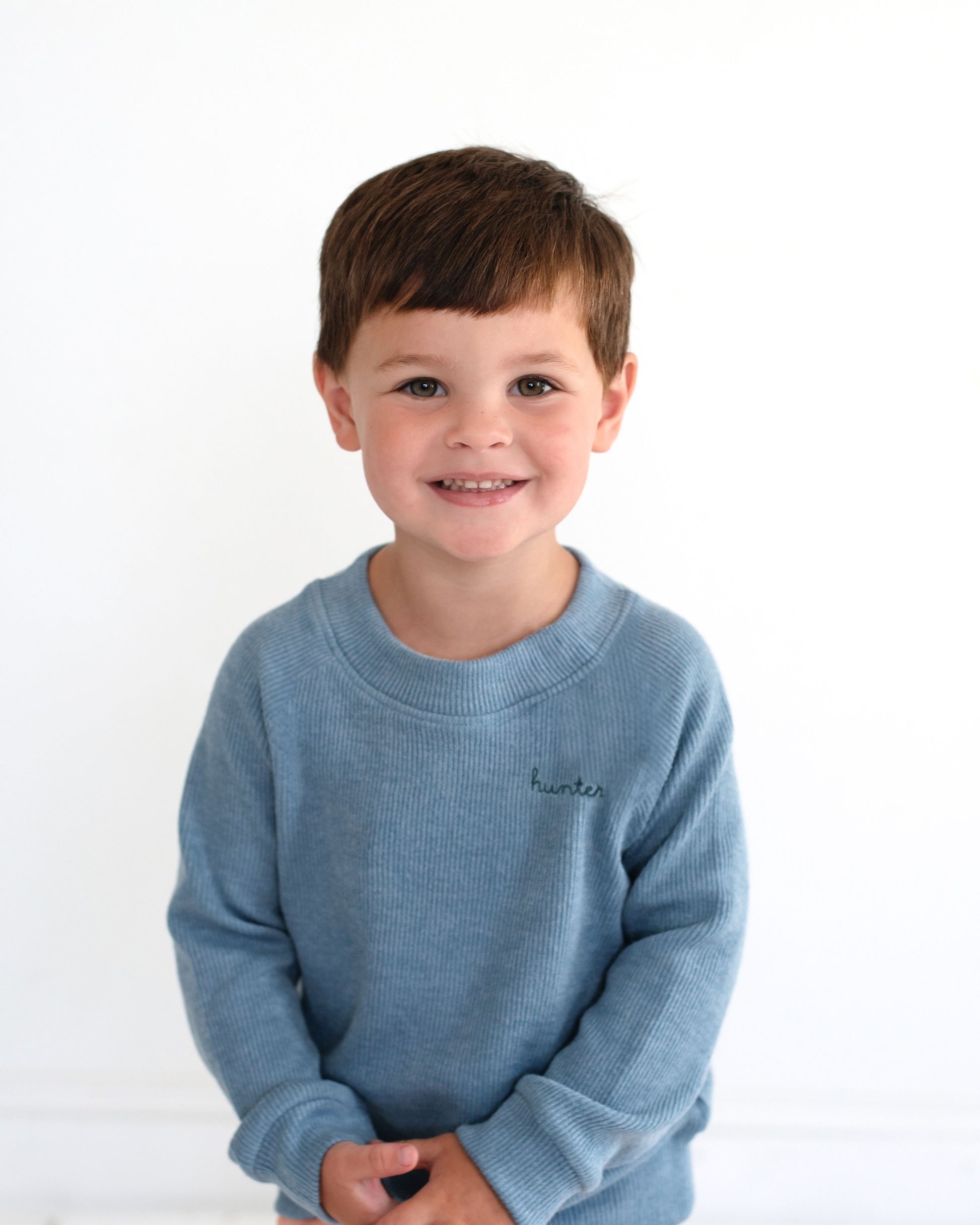 Young boy wearing a blue sweater with a brand logo on a white background