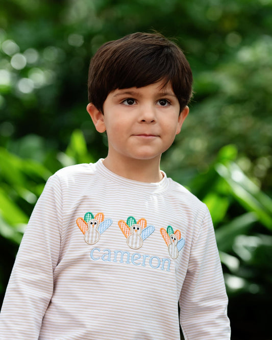 Young boy wearing a khaki shirt with appliques on it and a name embroidered
