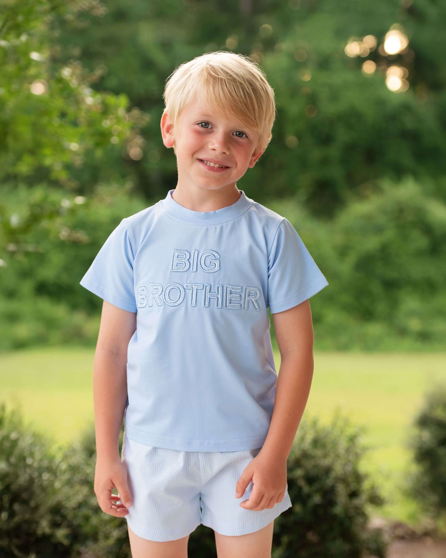Young boy wearing a light blue 'BIG BROTHER' shirt outdoors.