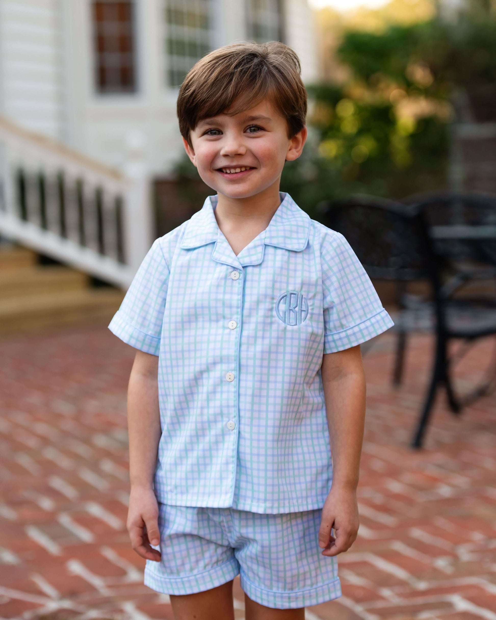Young boy wearing a light blue checkered outfit standing on a brick patio.