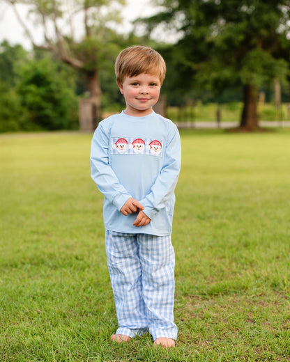 Young boy wearing a light blue long-sleeve shirt and checkered pants standing in a grassy field.