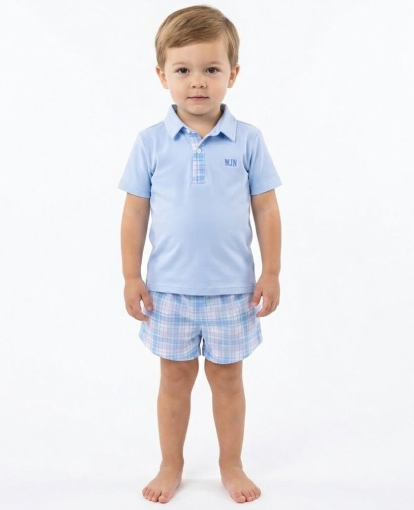 Young boy wearing a light blue polo shirt and checkered shorts on a white background