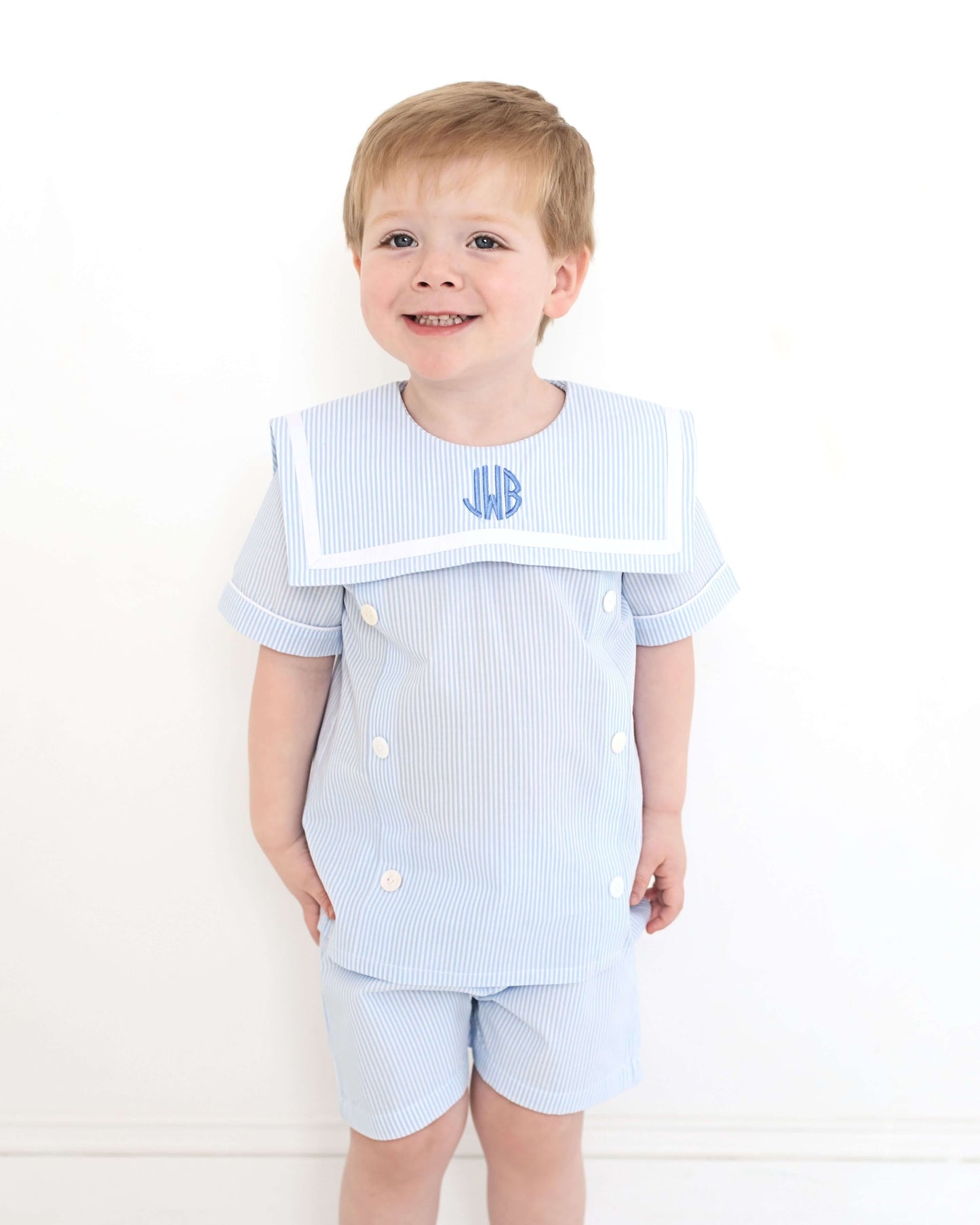 Young boy wearing a light blue striped outfit with a monogram on a white background