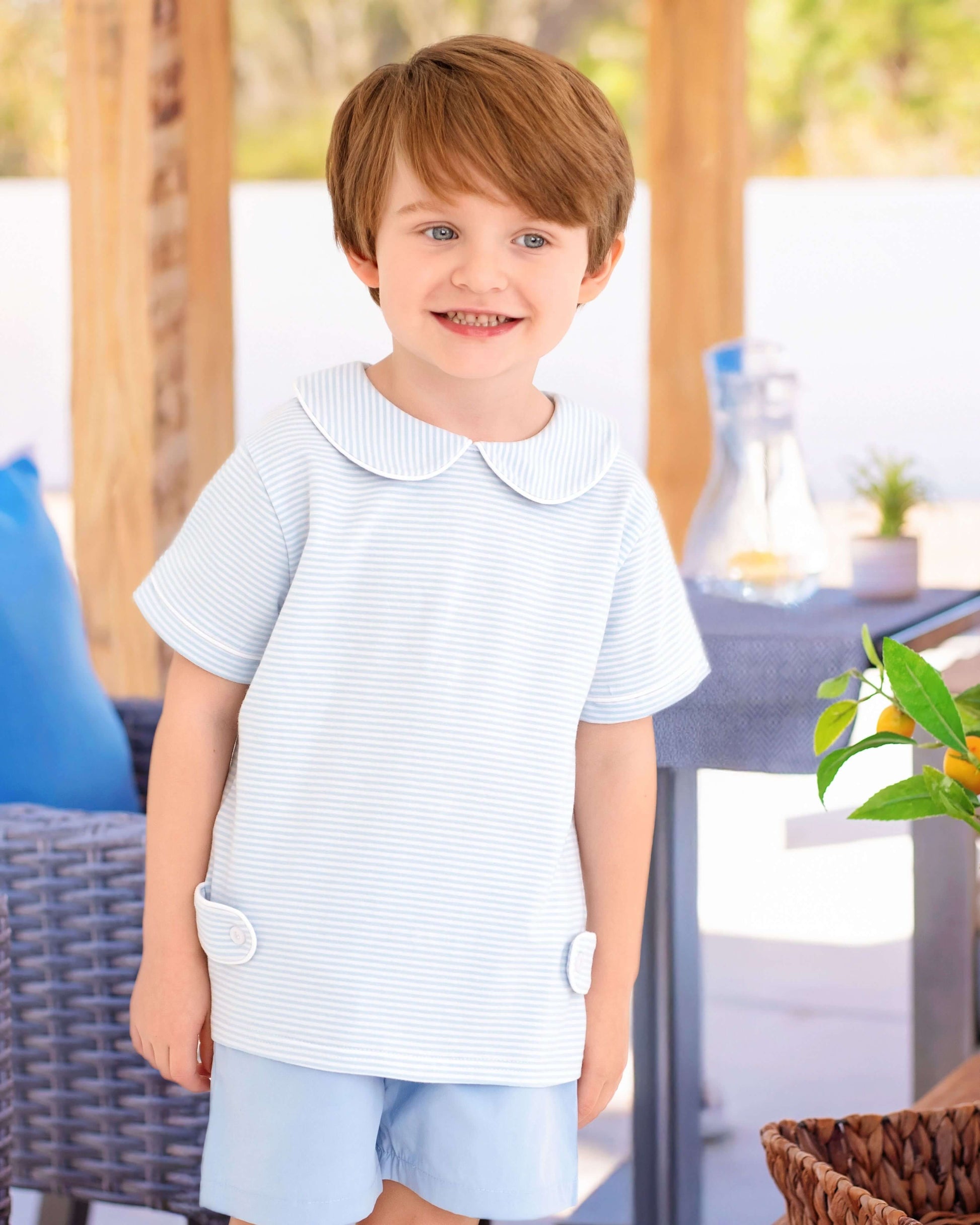Young boy wearing a light blue striped shirt with a collar outdoors.