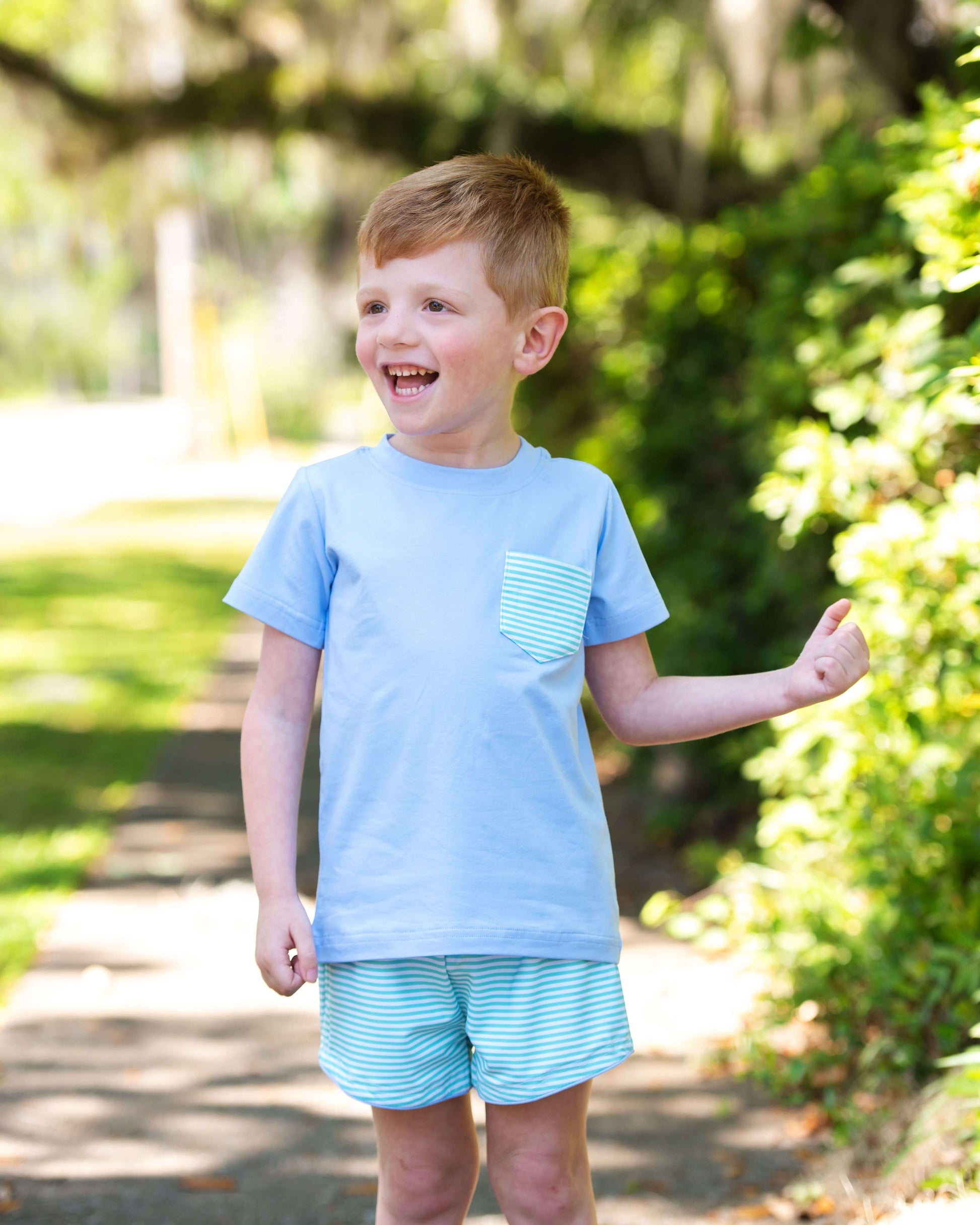 Young boy wearing a light blue t-shirt and striped shorts outdoors.