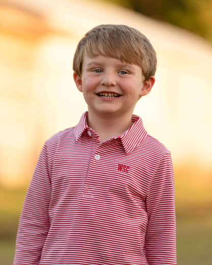 Young boy wearing a red and white striped shirt with a logo, standing outdoors with a blurred background.