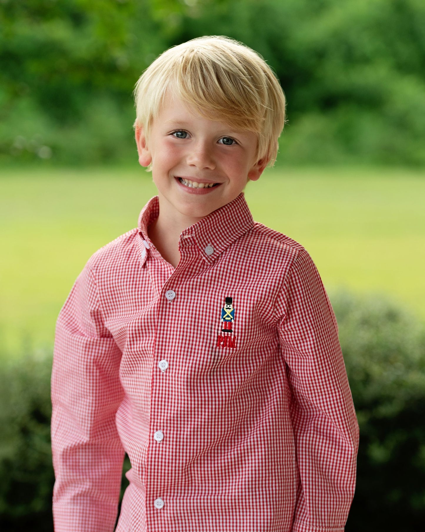 Young boy wearing a red checkered shirt with a small embroidered design outdoors.