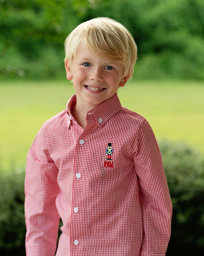 Young boy wearing a red checkered shirt with a small embroidered design outdoors.