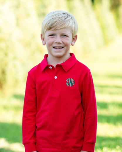 Young boy wearing a red polo shirt with a logo outdoors