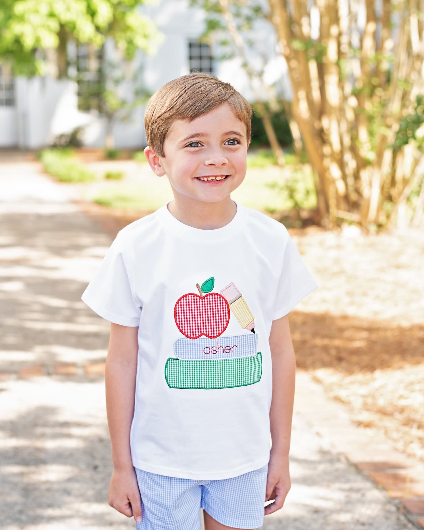 Young boy wearing a shirt with books, pencil and an apple. 