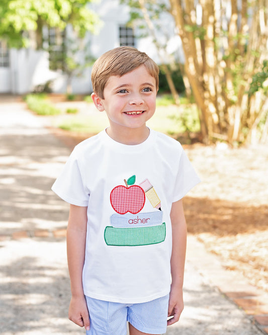 Young boy wearing a shirt with books, pencil and an apple. 