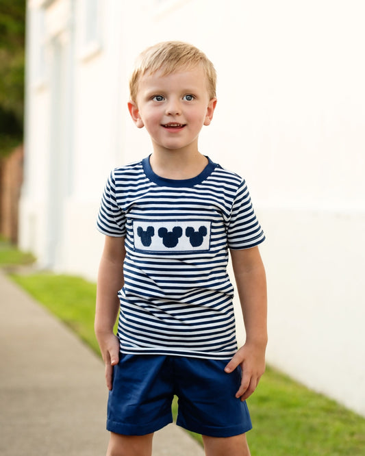 Young boy wearing a striped shirt with Mickey Mouse icons and navy shorts outdoors.