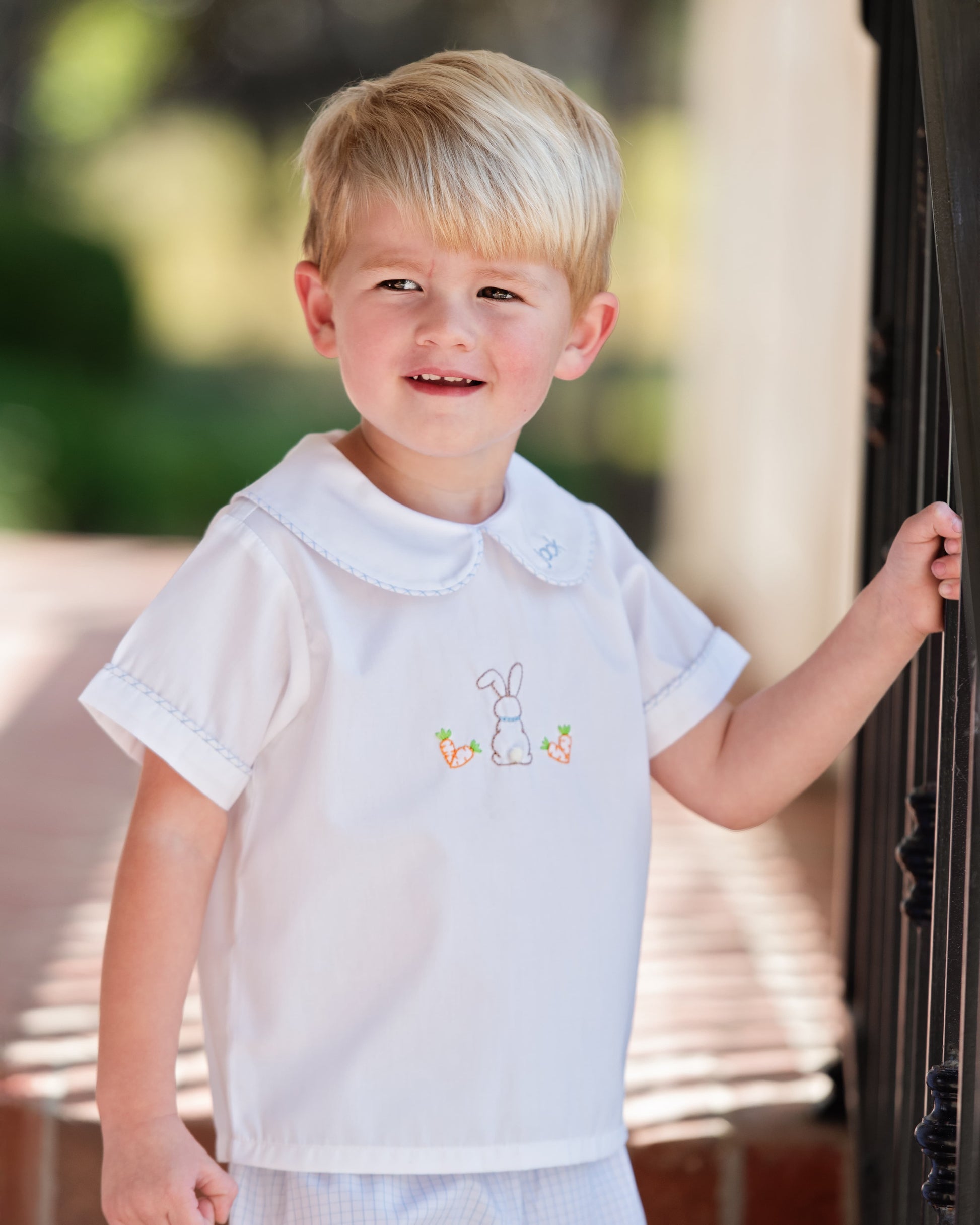 Young boy wearing a white shirt with embroidery, standing outdoors.