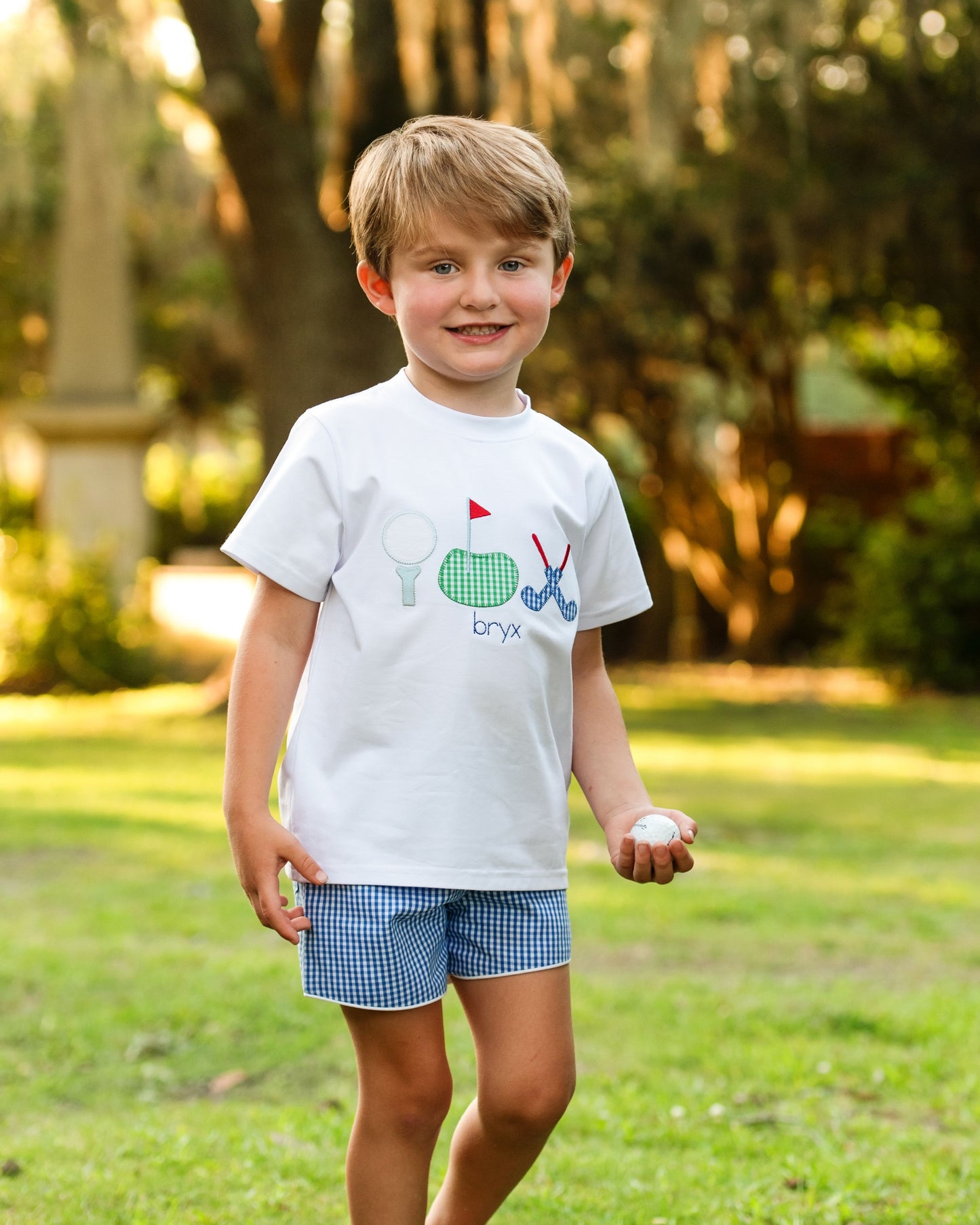 Young boy wearing a white t-shirt with graphics and text, standing outdoors on grass.