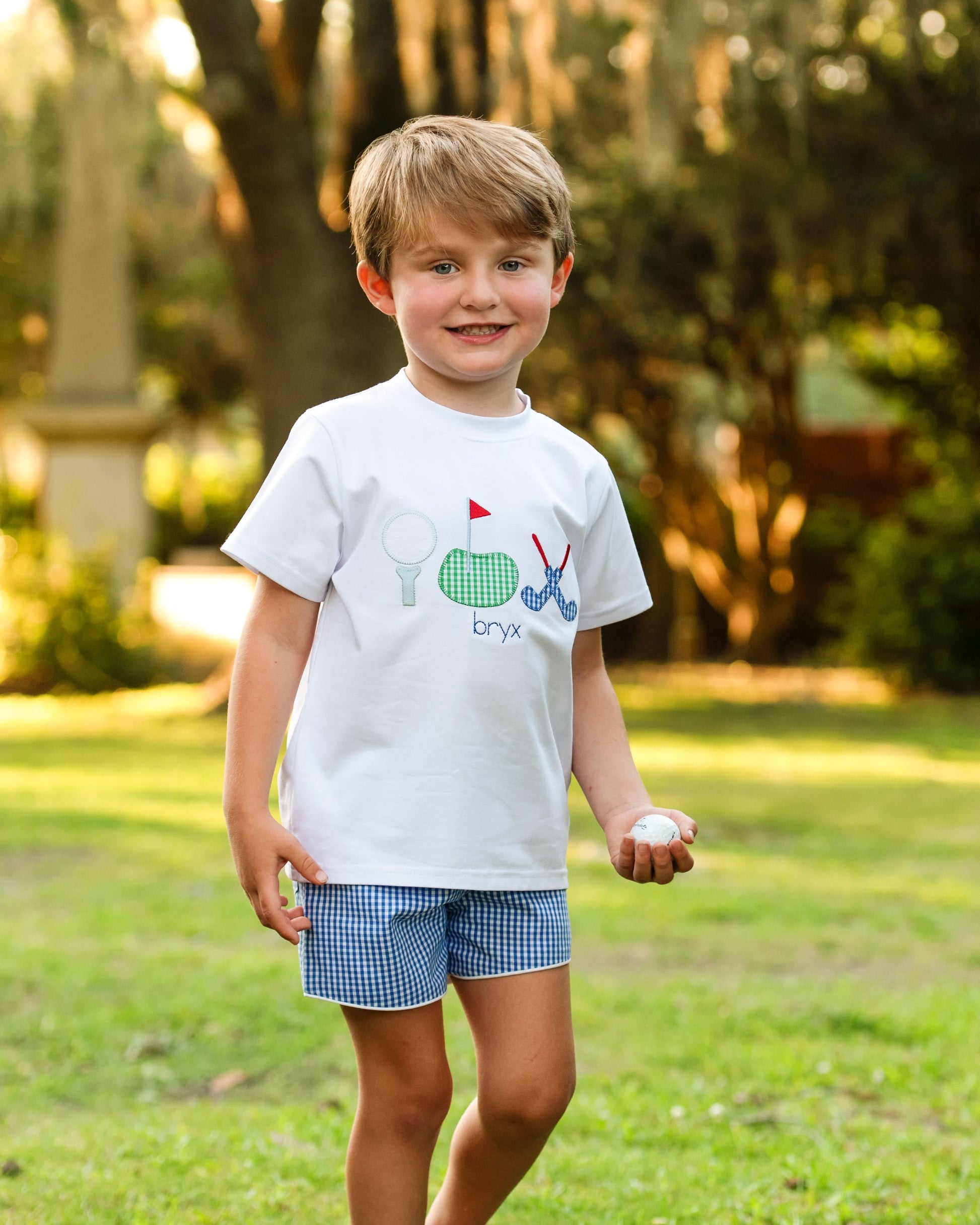 Young boy wearing a white t-shirt with graphics and text, standing outdoors on grass.
