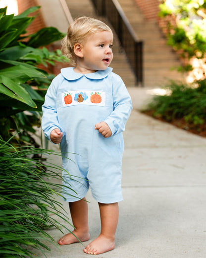 Young boy wearing blue short romper with smocked pumpkins and a turkey 