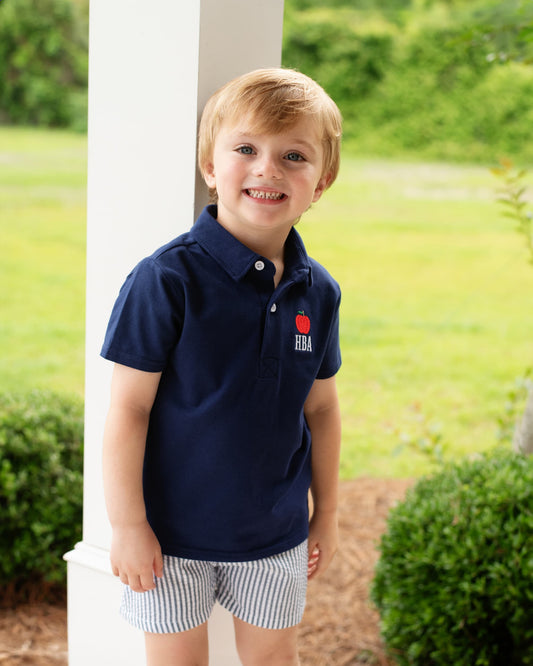 Young boy wearing navy striped shorts and a navy polo with an apple embroidered.