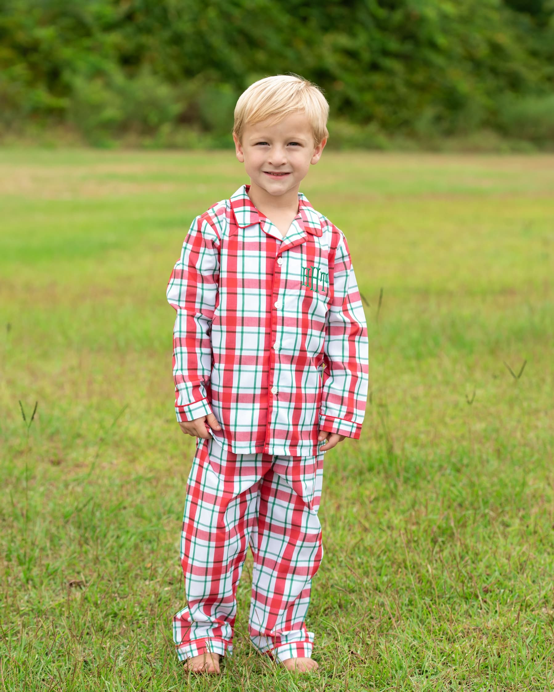 Young boy wearing red and white plaid pajamas standing in a grassy field.