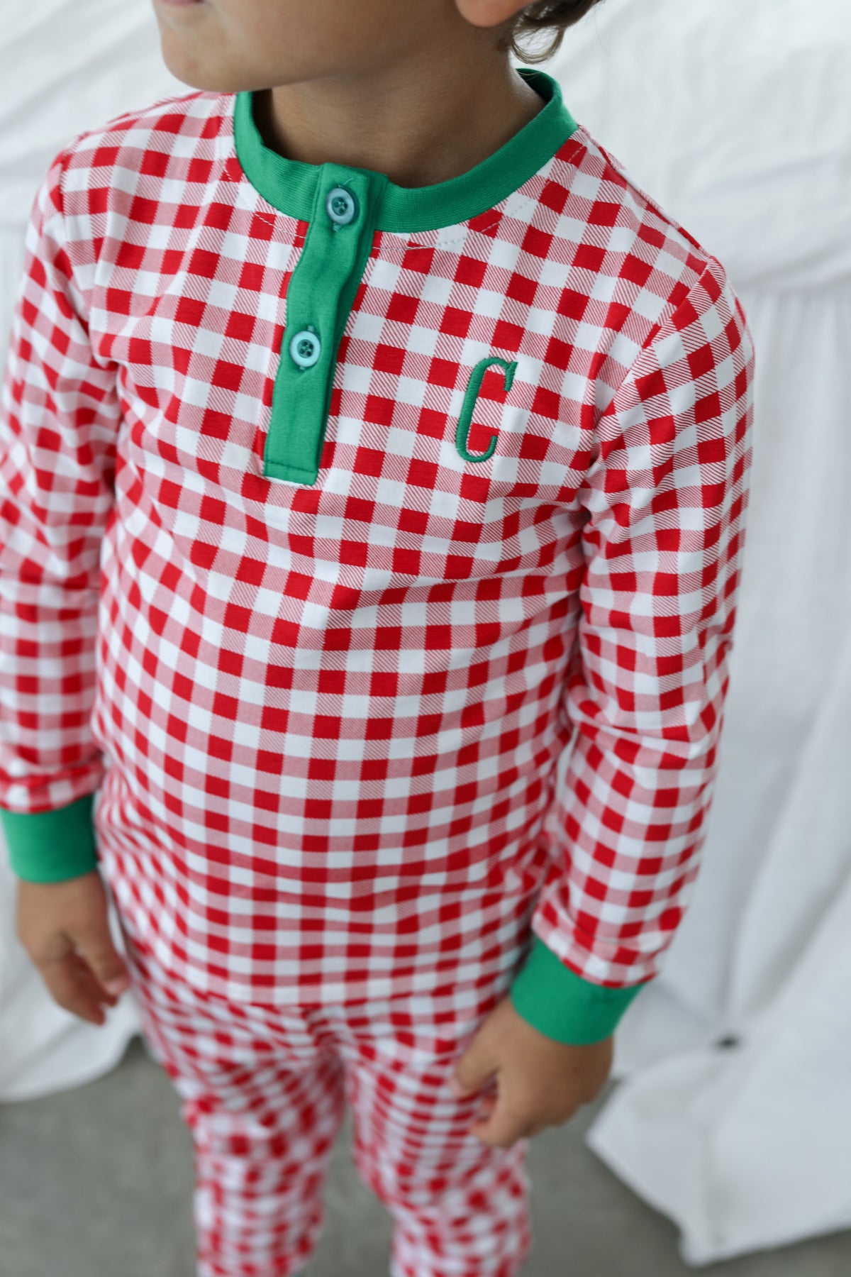 Young boy wearing red checked pajamas with green trim and a single letter monogram