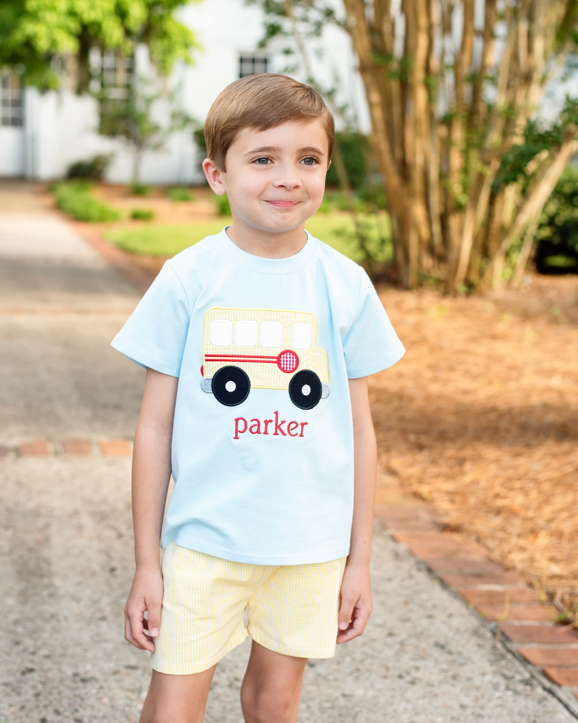 Young boy wearing yellow shorts and a school bus shirt.