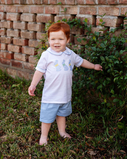 Young boy with red hair standing outdoors near a brick wall and greenery