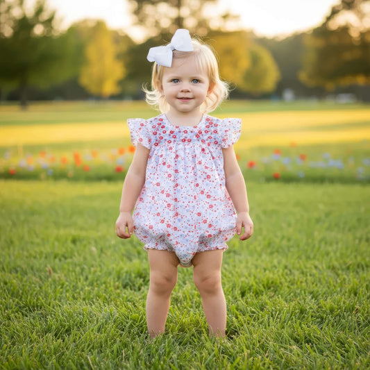 Young child in a floral romper standing in a grassy field with flowers.