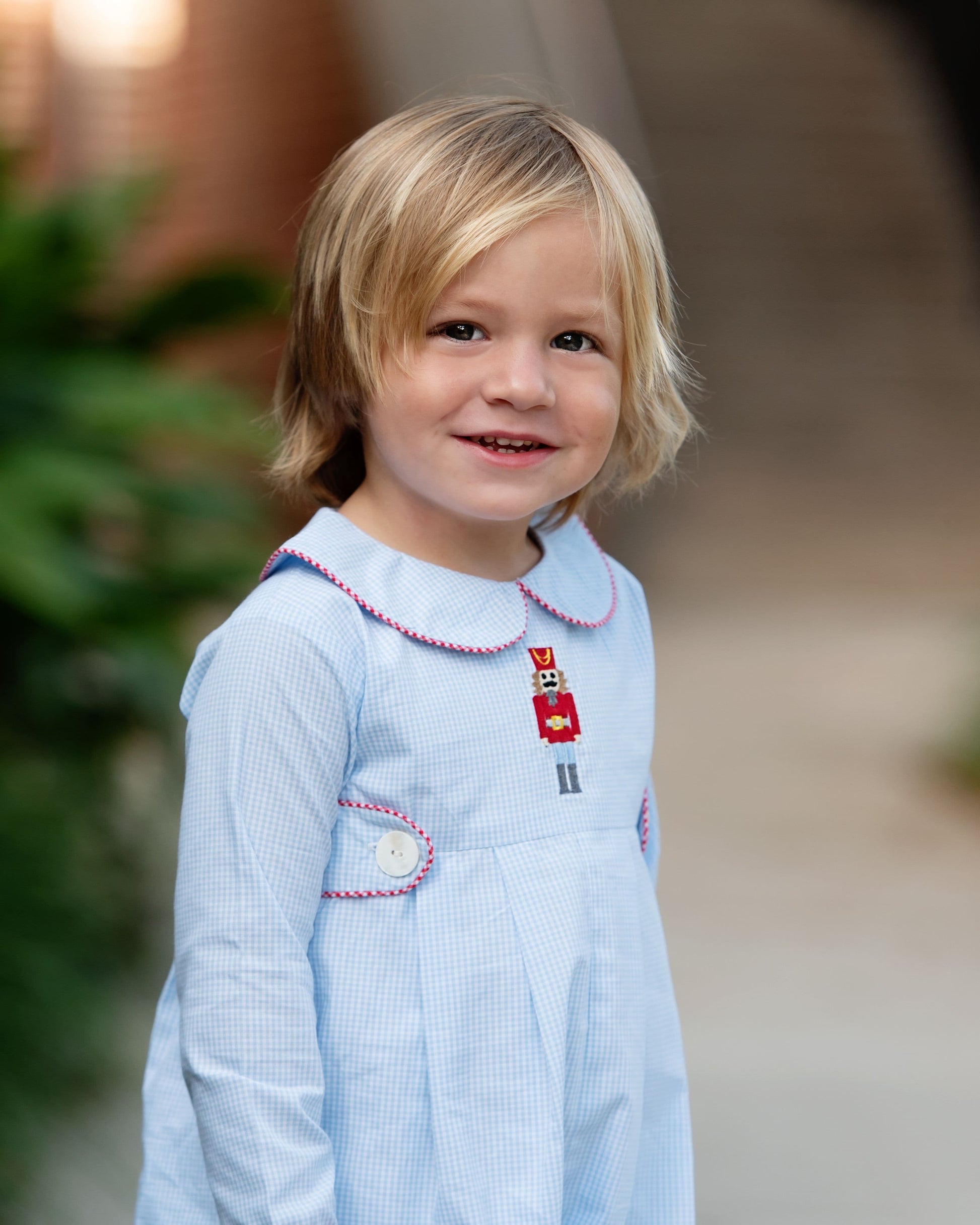 Young child wearing a light blue long romper with a blurred outdoor background