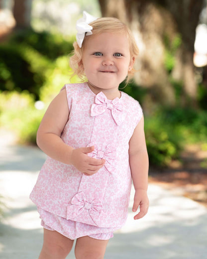 Young child wearing a pink floral outfit with a bow, standing outdoors.