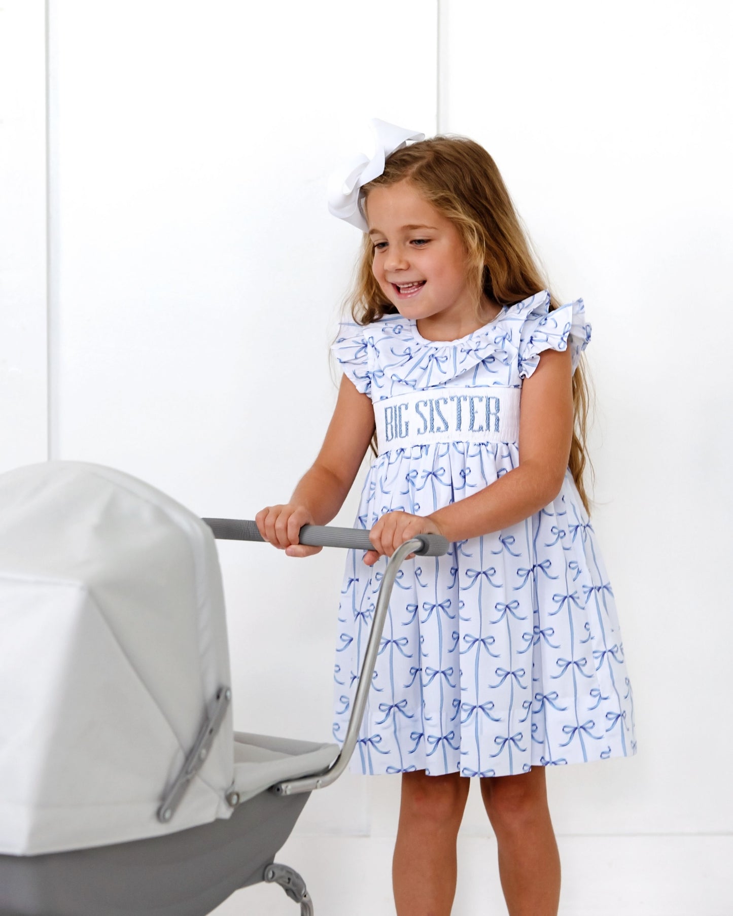 Young girl in a 'Big Sister' dress pushing a baby stroller against a white background